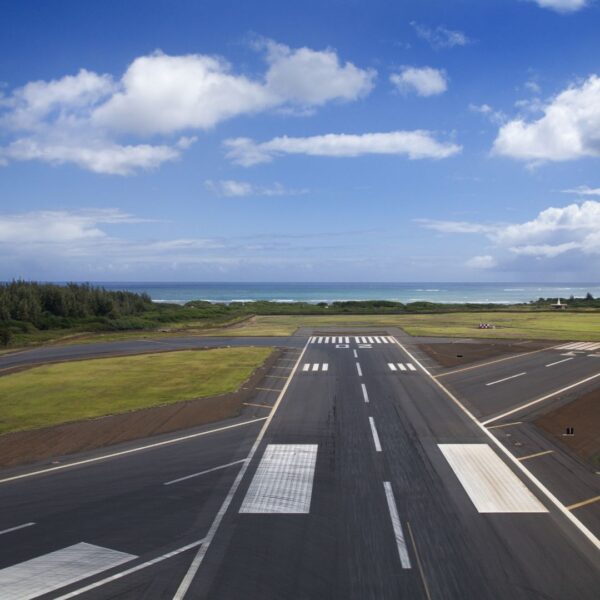 An airplane landing over turquoise waters near a tropical island.